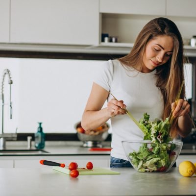 Young woman making salad at the kitchen